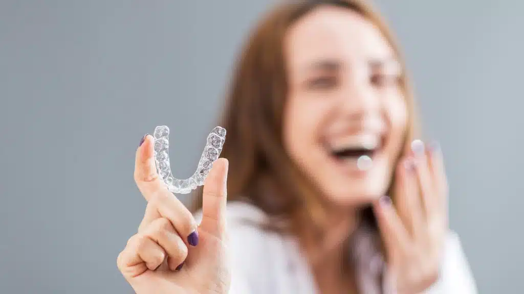 female smiling while holding clear aligners